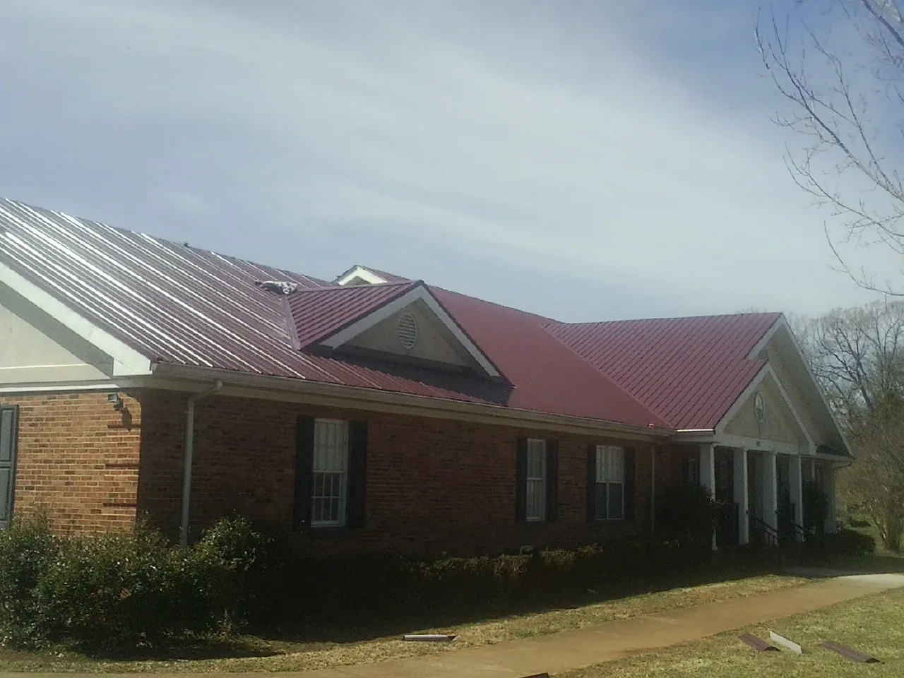 Red metal roof with gabled entries on a long brick building, from a Hail Damage Roof Repair job in Roosevelt