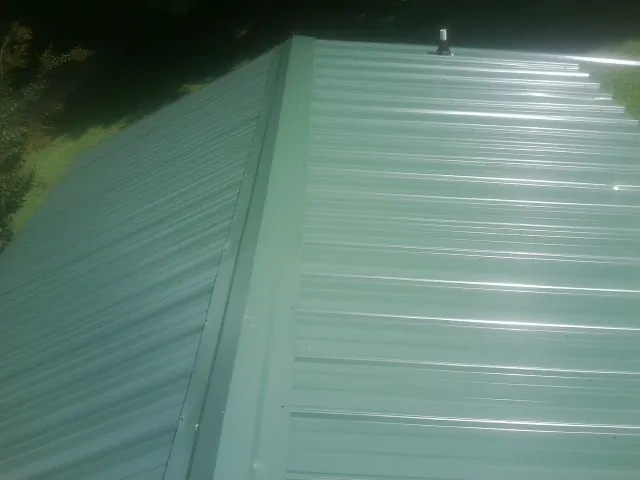 New green metal panels meeting at the ridge of a roof — Flat Roof Repair work by our crew in Roosevelt