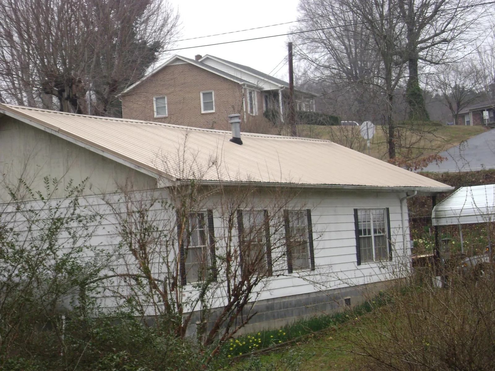 Tan metal roof on a white sided house set into a hillside — Commercial Roofing by Roofing Brothers in Roosevelt